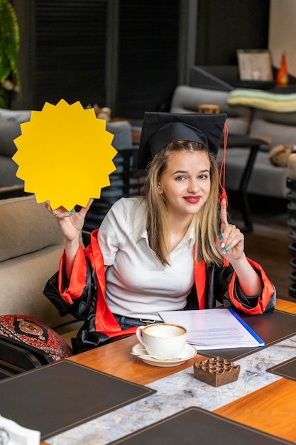 Mladá studentka má na sobě promoční plášť a drží krabici s nápady v restauraci
