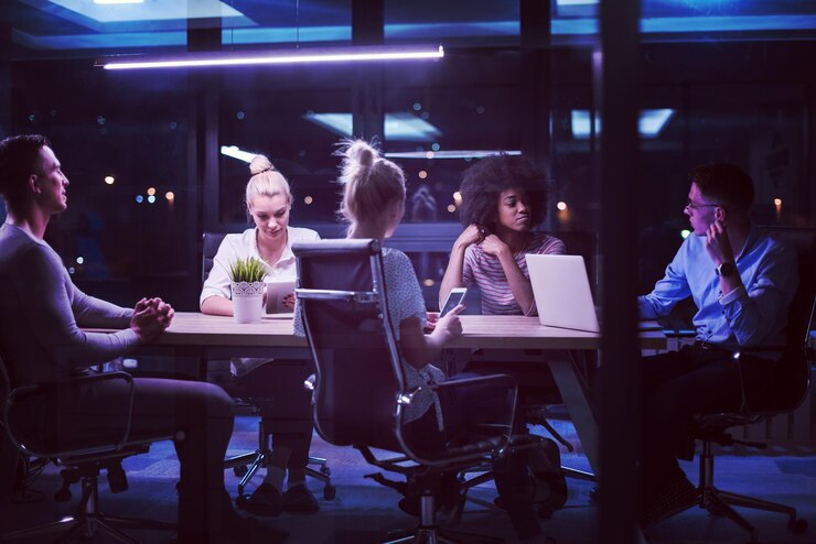 Multietnický startupový tým na schůzce v moderní noční kanceláři, brainstorming, práce na notebooku