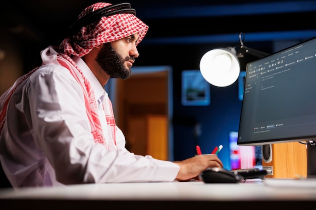 Muslim man types code on a desktop PC He excels in app programming and showcases his expertise in software development and algorithms This image represents the evolving world of digital technology