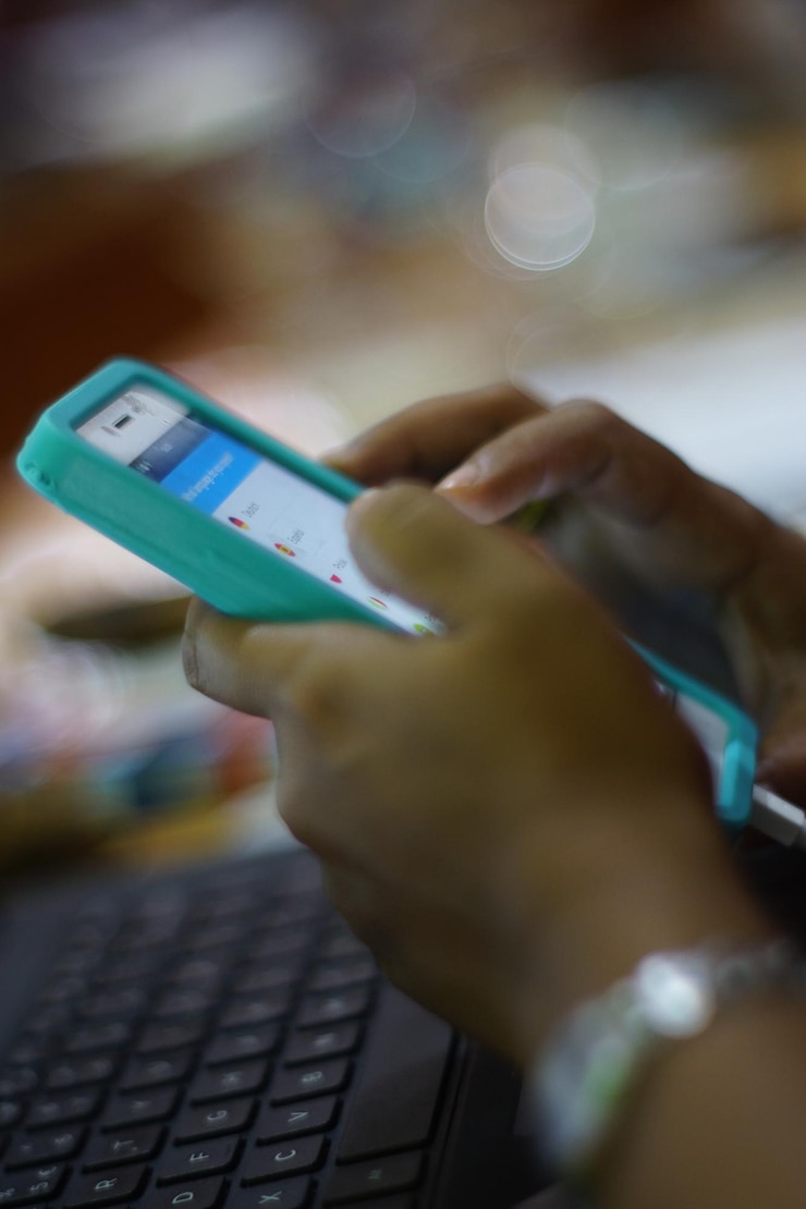 Fotografie oříznuté ruce ženy používající chytrý telefon nad notebookem