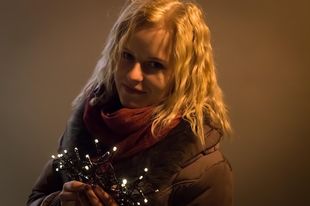 portrait of beautiful young woman holding illuminated string lights against wall