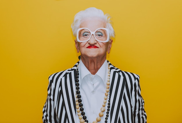 portrait of stylish senior woman standing against yellow background