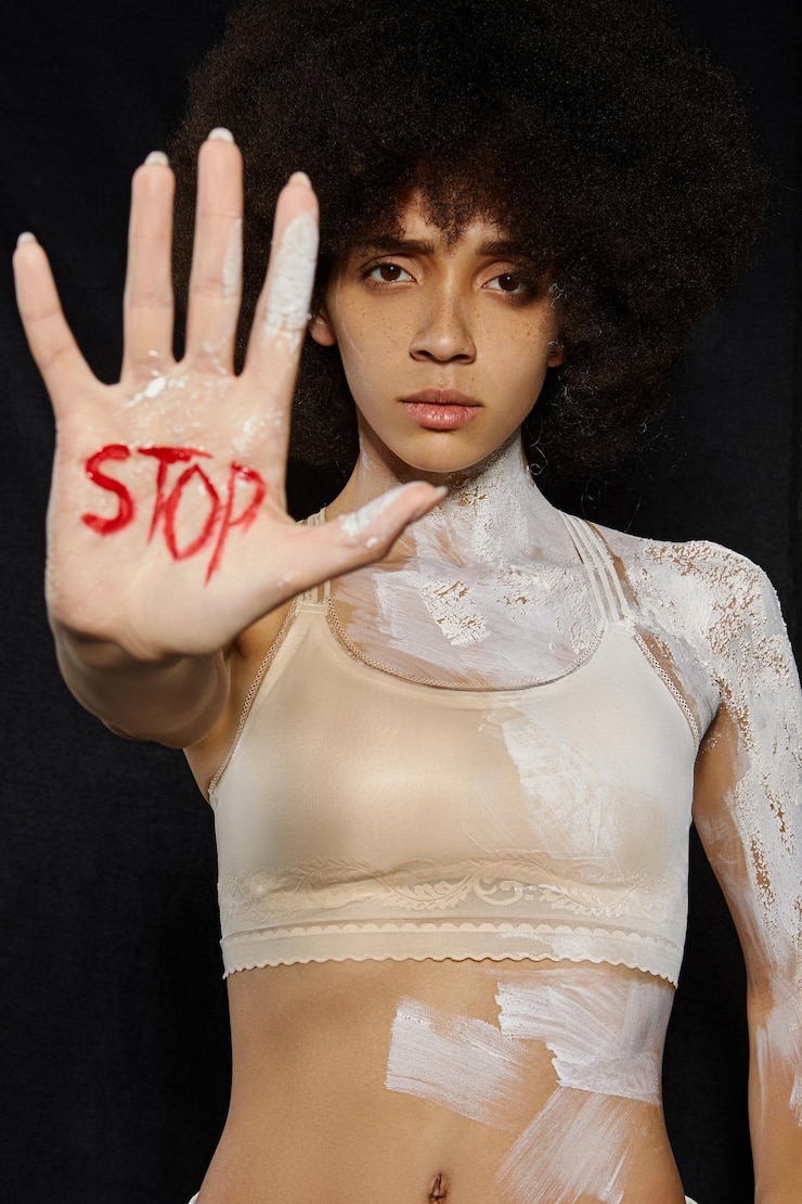 Fotografie portrait of woman with paint showing stop gesture with text while standing against black background