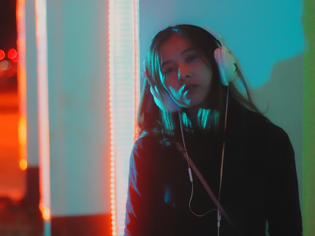 portrait of young woman listening music against illuminated wall