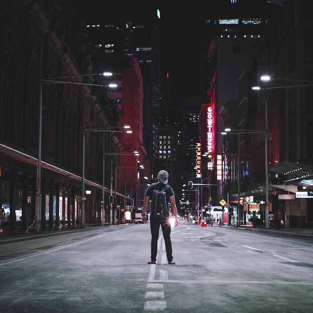 rear view of man standing on street amidst buildings at night