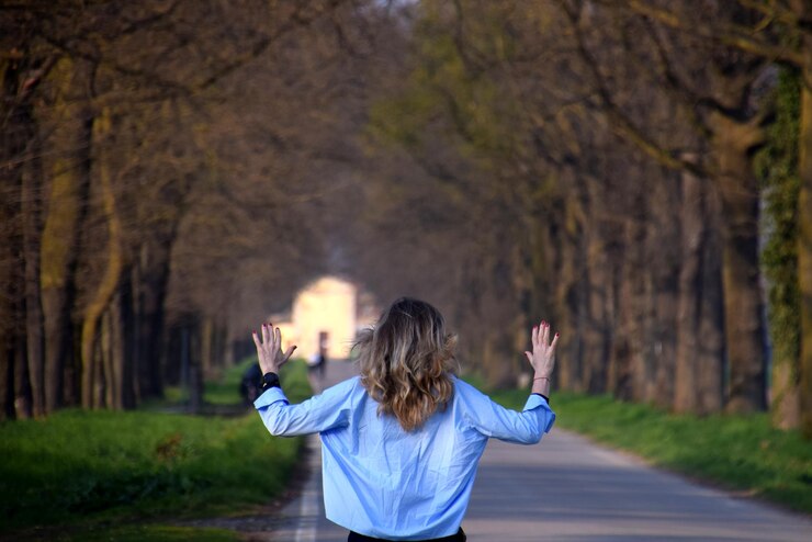 Fotografie rear view of woman with arms raised standing on footpath against trees