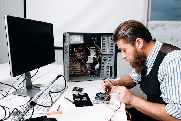 Repairman welding computer circuit in workshop. Bearded engineer fixing electronic component. Repair, development, technology concept