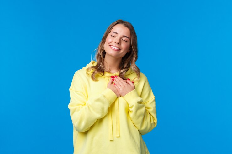Fotografie romantic alluring blond caucasian girlfriend in yellow hoodie, press hands to heart and close eyes
