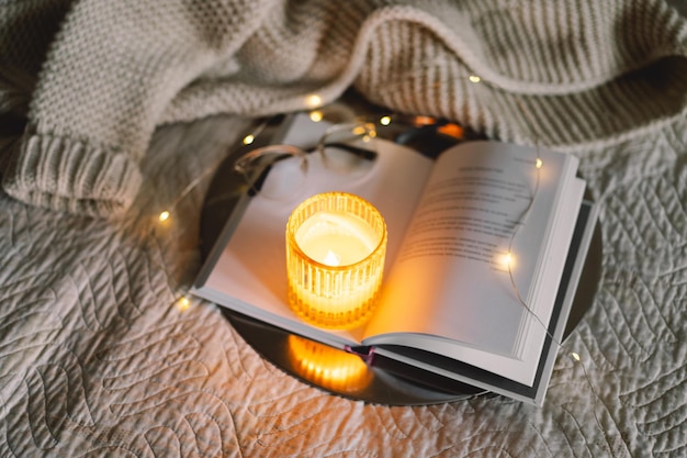 scented candle with an open book in bed with a warm blanket