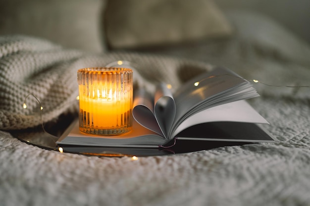 scented candle with book with folded sheets in heart shape in bed