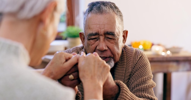 Senior couple holding hands and praying in home for religion hope or love for mindfulness Elderly man woman and support for peace prayer and gratitude for connection to God holy spirit or faith