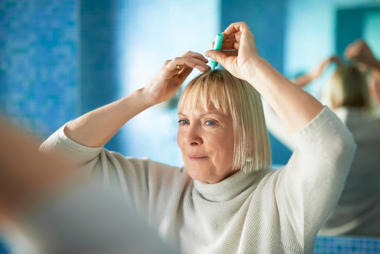 Fotografie senior woman applying liquid on blond hair reflecting on mirror at home