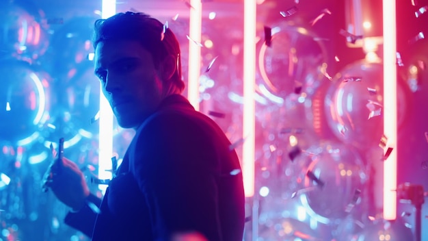 sexy man dancing under confetti in club guy smoking on neon lamps background