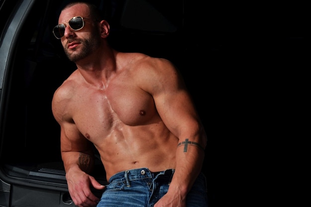 Shirtless muscular man leaning on car trunk