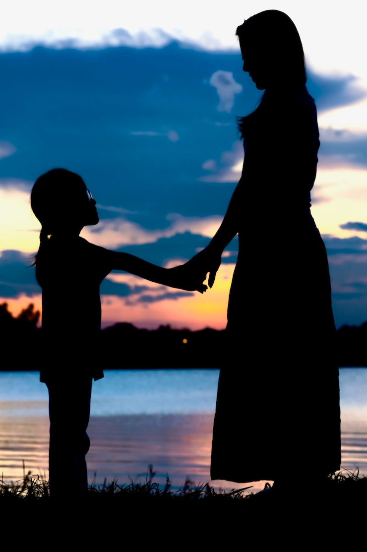 Fotografie silhouette mother holding hands of daughter while standing against lake during sunset