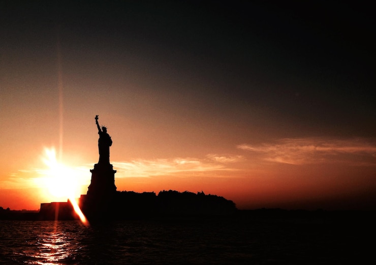 Fotografie silhouette statue of liberty in front of sea against sky during sunset