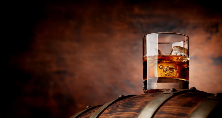 Fotografie sklenice whisky s kostkami ledu na starém sudu