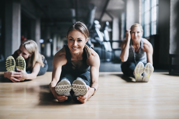 Fotografie stretching happy and women in gym for exercise training and warm up on floor for mobility sports friends and people for wellness health and flexibility for performance fitness and strength