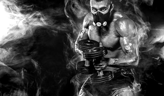 Svalnatý mladý fitness sportovec v tréninkové masce cvičí s činkou ve fitness posilovně.