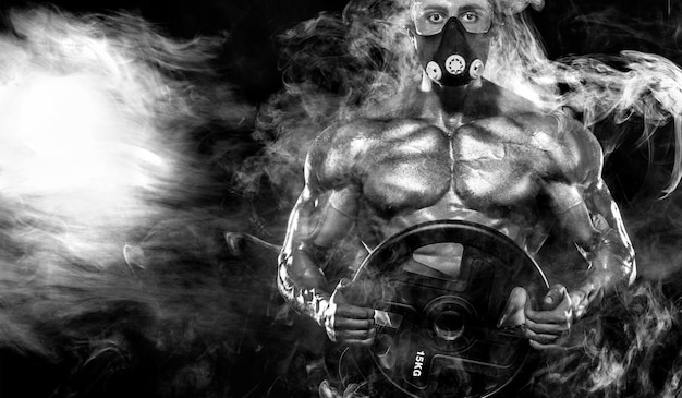 Svalnatý mladý fitness sportovec v tréninkové masce cvičí s činkou ve fitness posilovně.