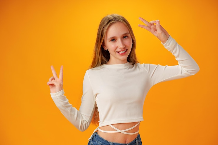 Fotografie teen girl makes peace or victory sign over yellow background