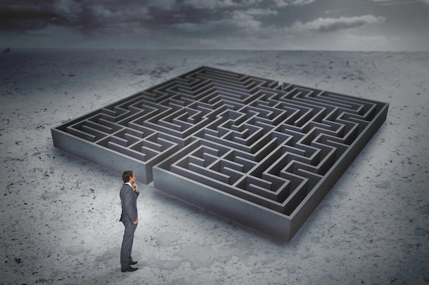 Thinking businessman against big maze under cloudy sky