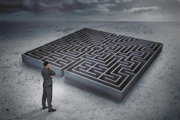 Thinking businessman against big maze under cloudy sky