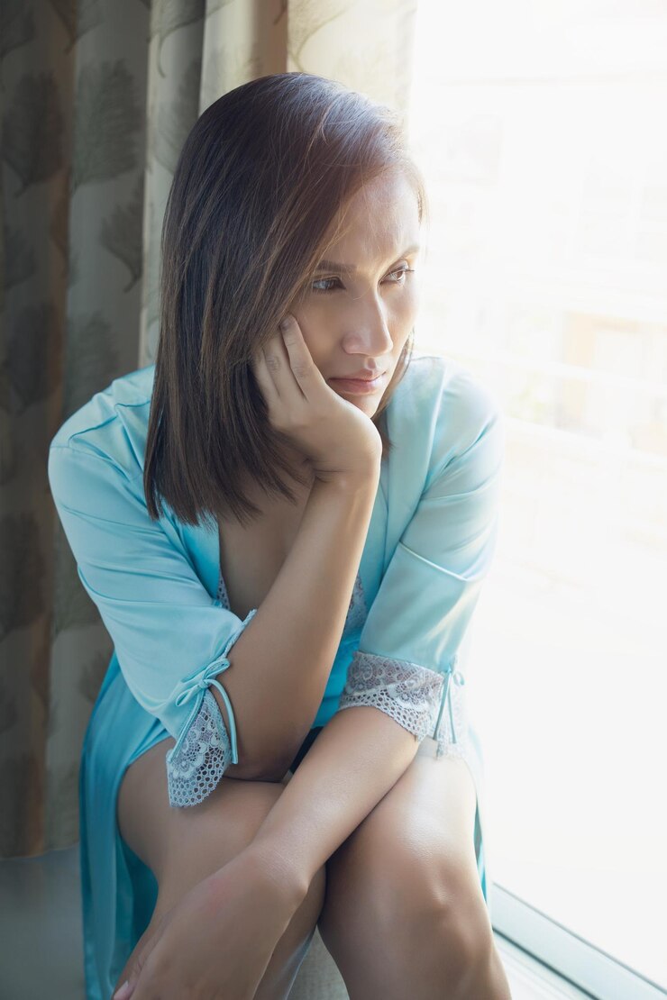 Fotografie thoughtful young woman looking through window while sitting at home