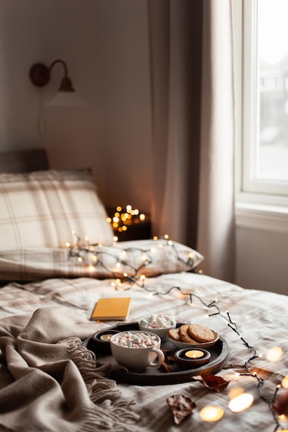 Warm cozy bedroom interior with cup of hot chocolate on tray candles christmas lights
