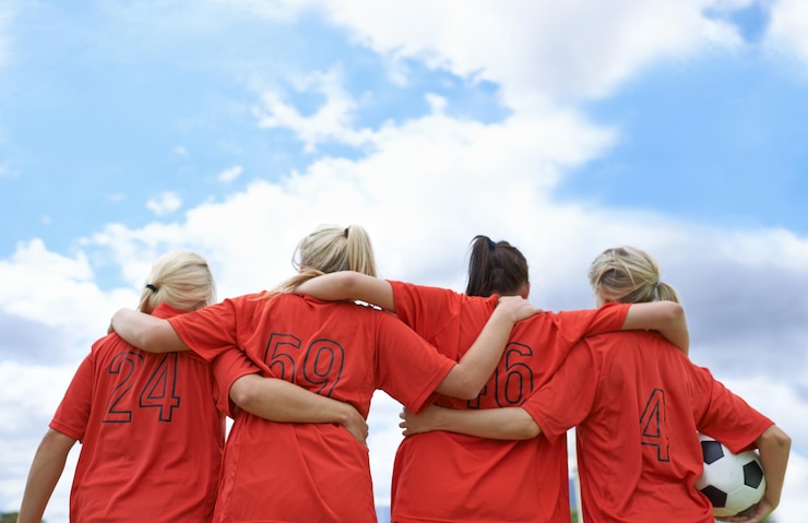 Fotografie woman hug and back of soccer team ready for sports match game or outdoor practice with blue sky rear view of female person or group of football players standing in unity with ball in nature