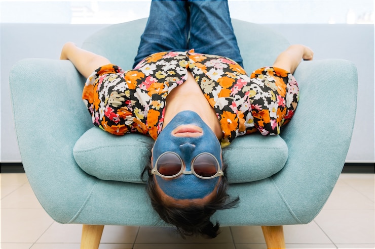 Fotografie woman with blue beauty mask and sunglasses in a turquoise armchair sitting upside down