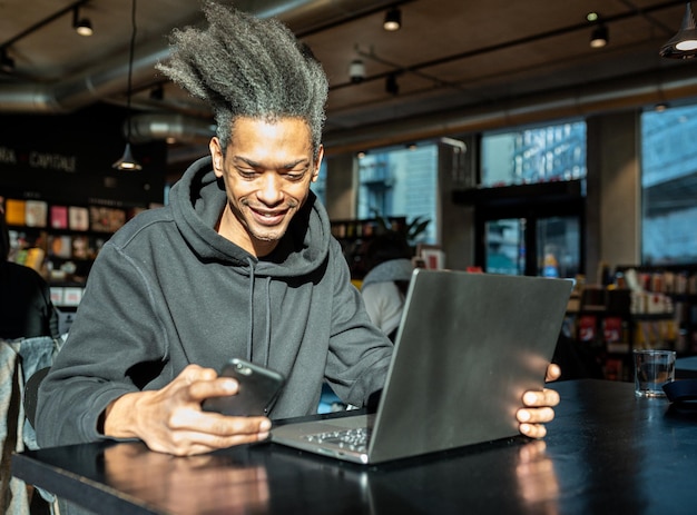 Young blogger creating contents for his blog with laptop and smartphone, young latin american working connected with modern  tecnology, lifestyle concept of connected working blogger
