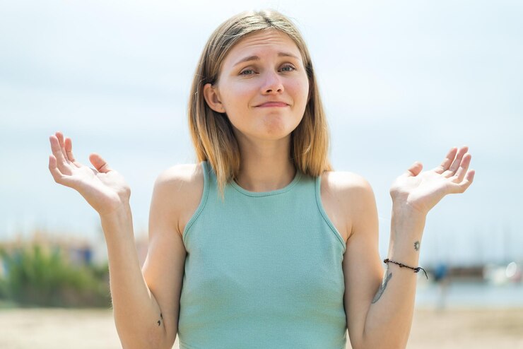 Fotografie young blonde woman at outdoors having doubts while raising hands