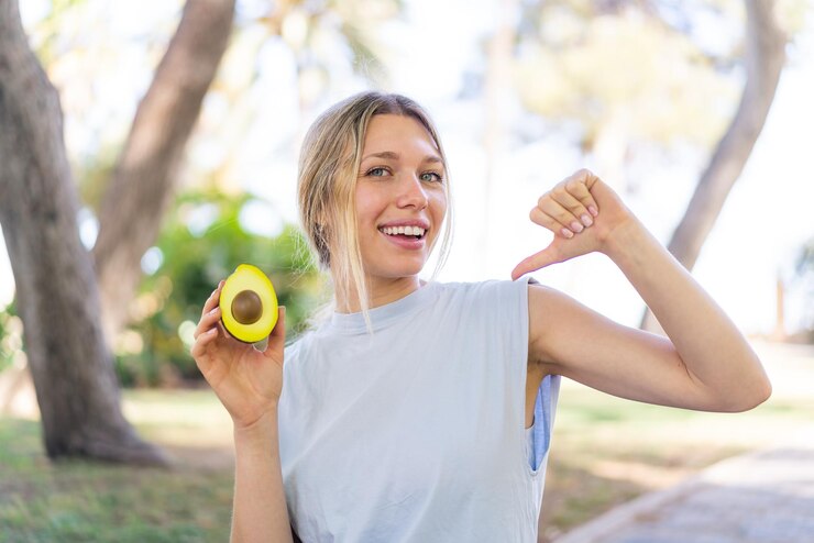 Fotografie young blonde woman holding an avocado at outdoors proud and selfsatisfied