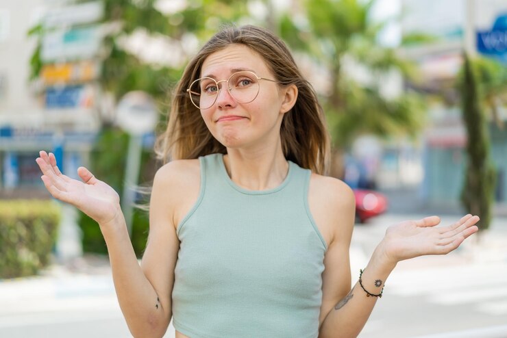 Fotografie young blonde woman with glasses at outdoors having doubts while raising hands