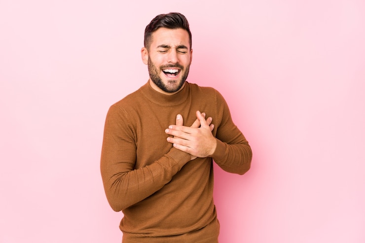 Fotografie young caucasian man against a pink wall isolated laughing keeping hands on heart, concept of happiness.