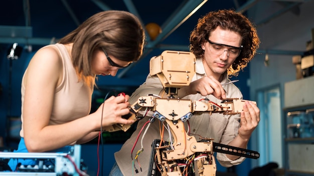 Young man and woman in protective glasses doing experiments in robotics in a laboratory Wooden robot