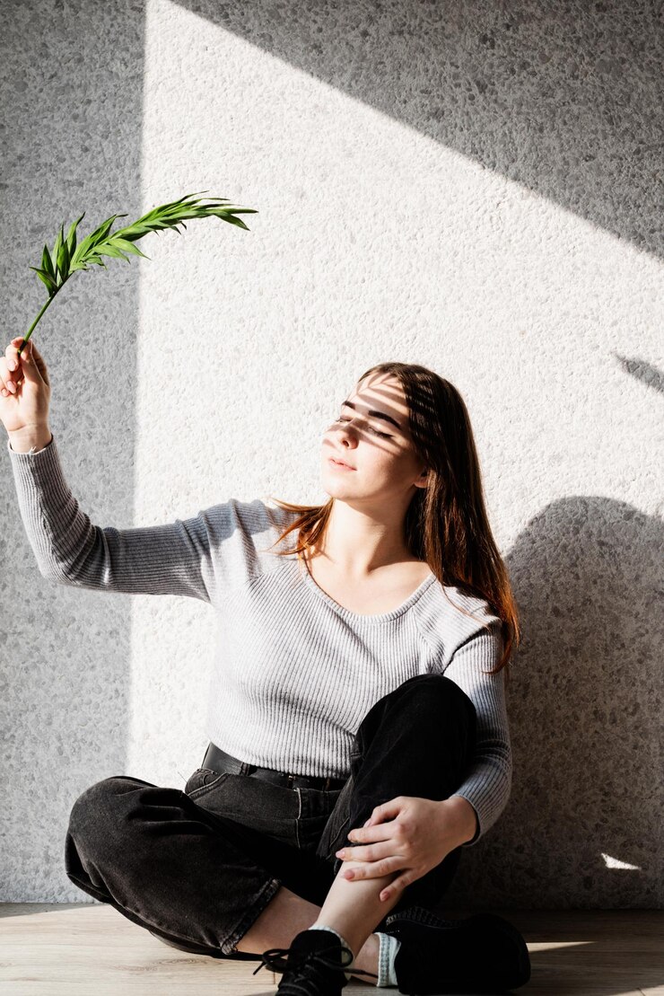 Fotografie young woman holding plant while sitting against wall outdoors