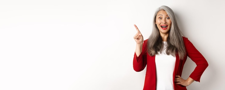Zdarma Fotografie business concept cheerful asian businesswoman with grey hair wearing red blazer and makeup pointing