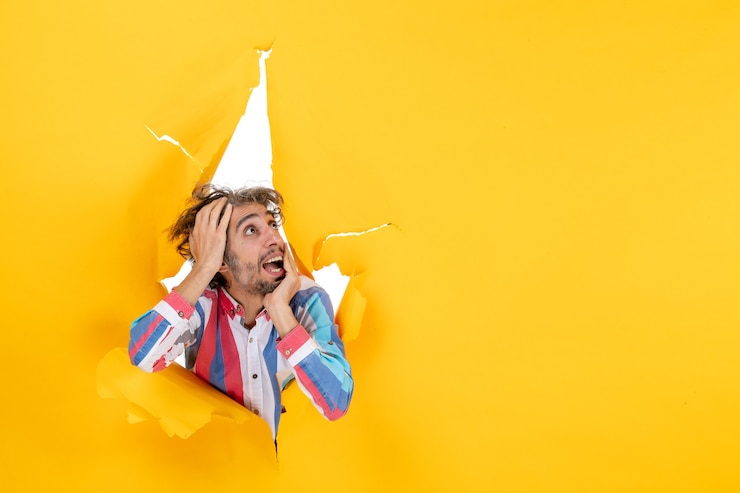 Zdarma Fotografie front view of an emotional and crazy young guy looking up through a torn hole in yellow paper