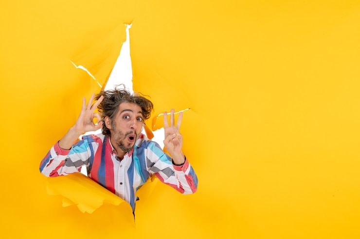 Zdarma Fotografie front view of an emotional and crazy young guy showing three through a torn hole in yellow paper