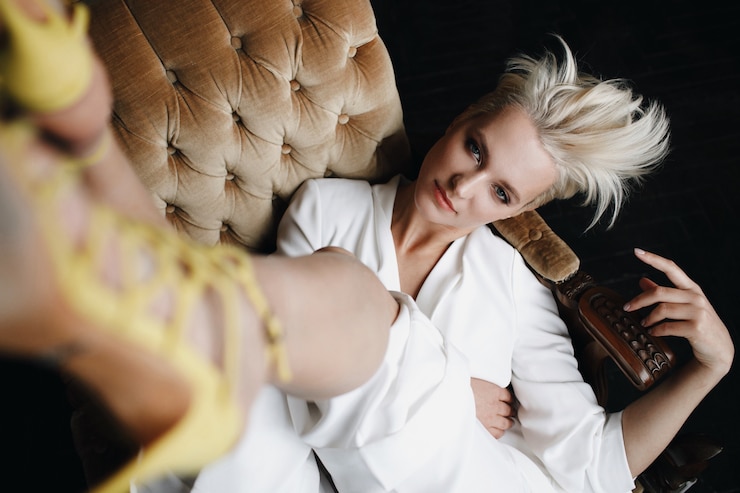 Zdarma Fotografie gorgeous blonde fashion model in white suit sits on a soft armchair holding her legs up