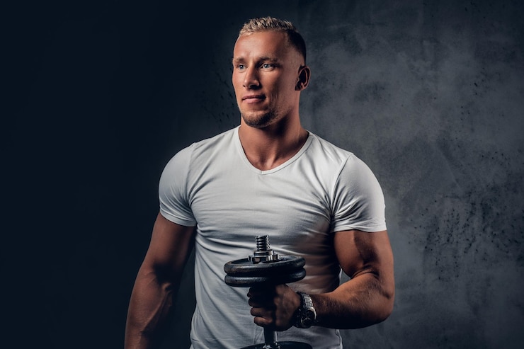 Zdarma Fotografie handsome muscular blond male in a white t shirt holds dumbbell over grey artistic background.