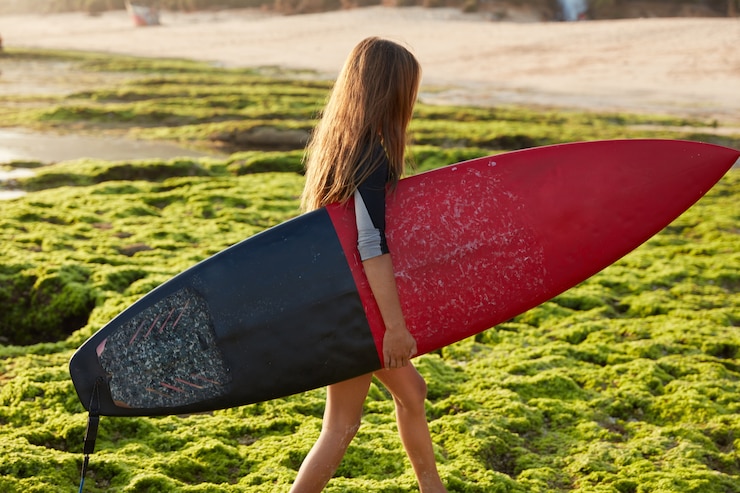 Zdarma Fotografie hobby and sport concept. active female surfer carries surf board, walks on coast during summer holidays, wants to hit ocean waves, has recreation in paradise place, poses alone. horizontal shot