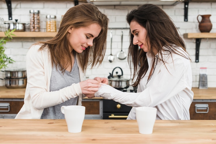 Zdarma Fotografie lesbian woman buttoning her girlfriend's shirt shelves in the kitchen