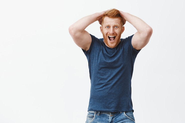 Zdarma Fotografie man yelling from regret and shock. handsome mature redhead guy in despair, touching hair, screaming and staring shocked and devestated, feeling disappointment over gray wall