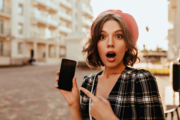 Zdarma Fotografie ohromená elegantní žena drží smartphone na ulici. venkovní fotografie šokované emotivní dívky v červeném baretu.