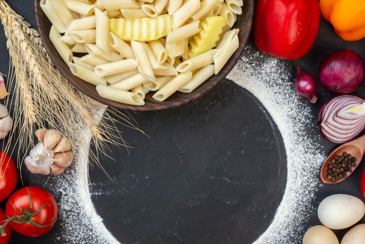 Zdarma Fotografie pohled shora na rozsypaný kruh mouky, penne těstoviny s bramborem v misce, červenou cibuli, rajčata, česnek, pšeničné klasy na stole