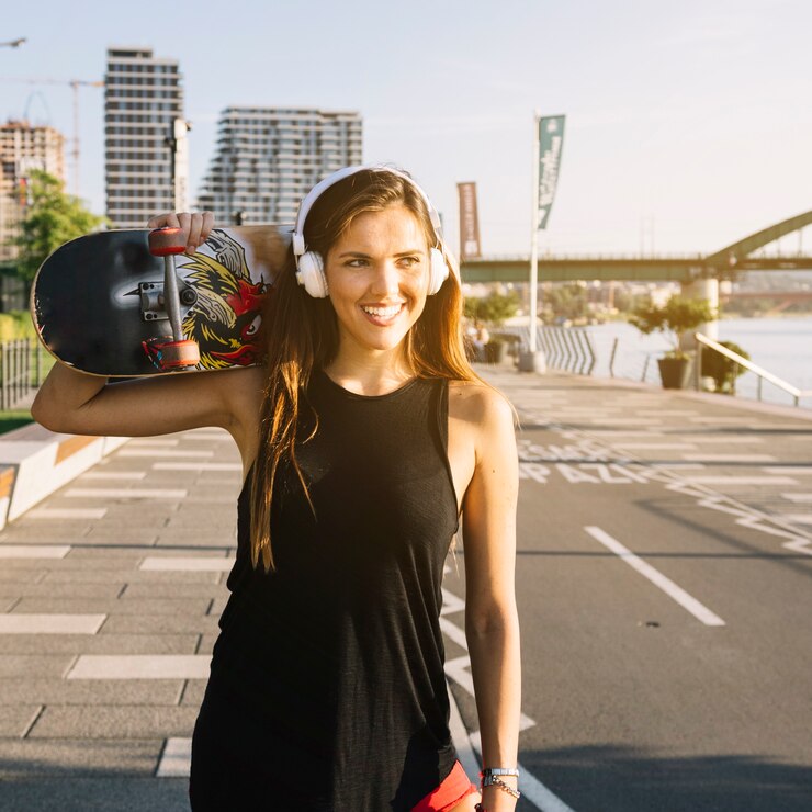 Zdarma Fotografie portrait of a happy woman with skateboard listening to music on headphone