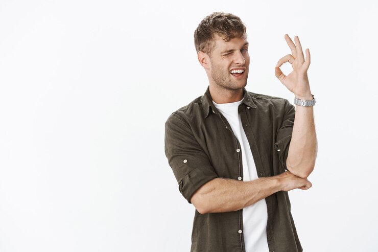 Zdarma Fotografie portrait of charismatic boyfriend winking and showing okay gesture as assuring he got everything under control and understood standing intriguing and hinting over grey wall